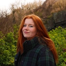 Image of female student with red hair in green and navy checked coat outdoors